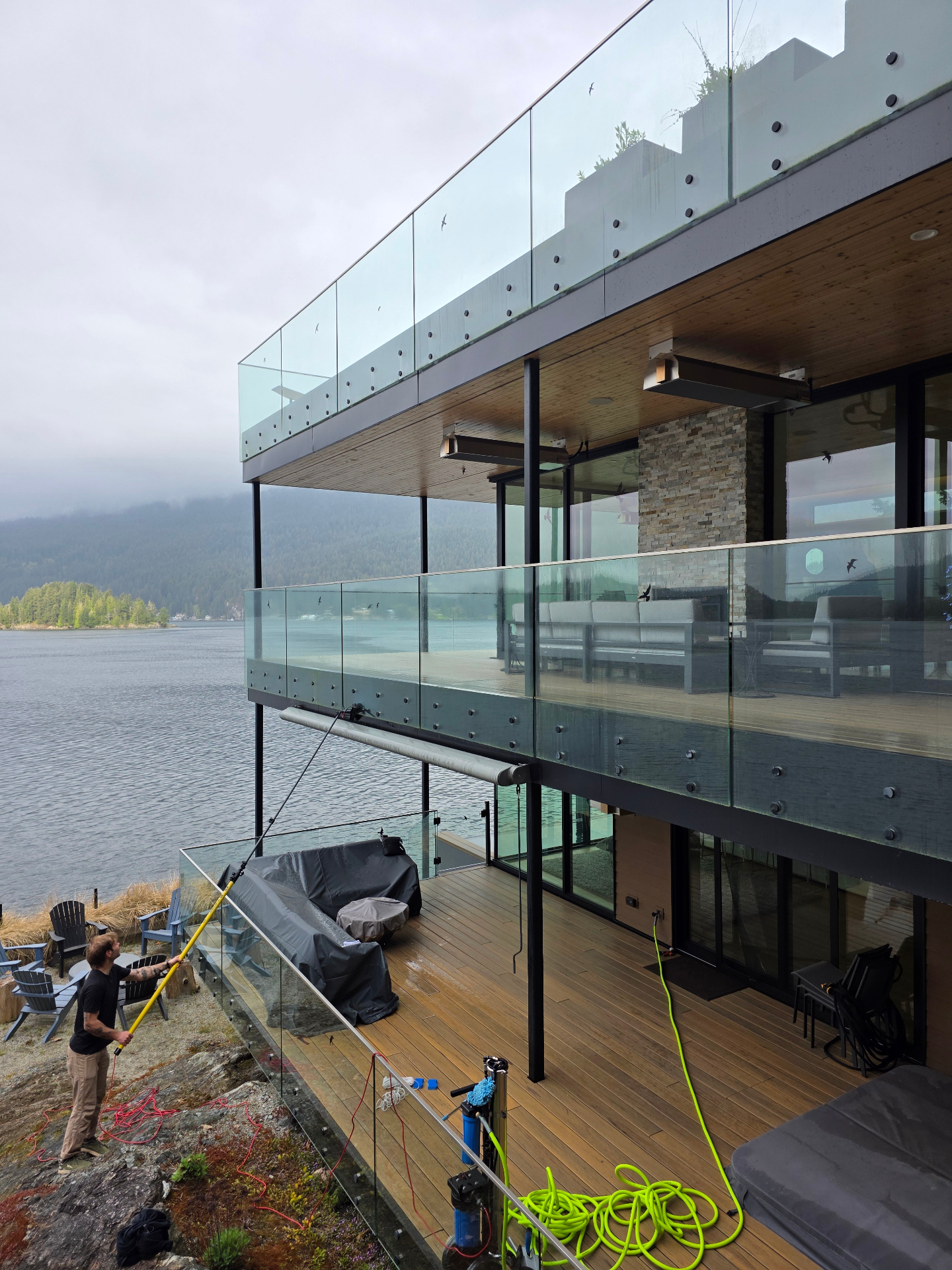 Complete Window Cleaning technician using a fed-pole to wash three stories of glass on a modern North Shore waterfront home